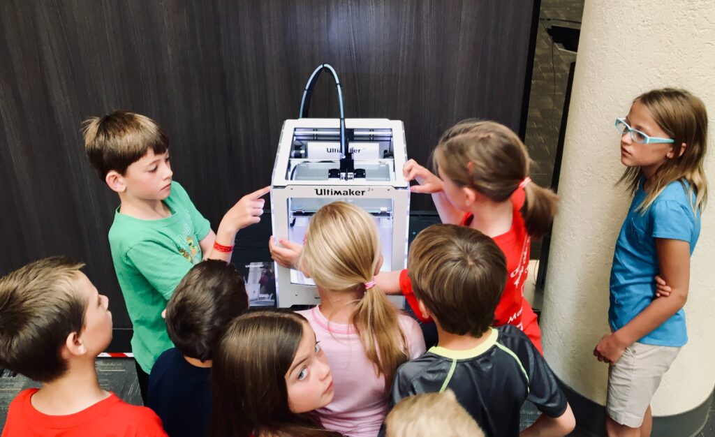 Eine Gruppe von Kindern steht begeistert vor einem 3-D Drucker