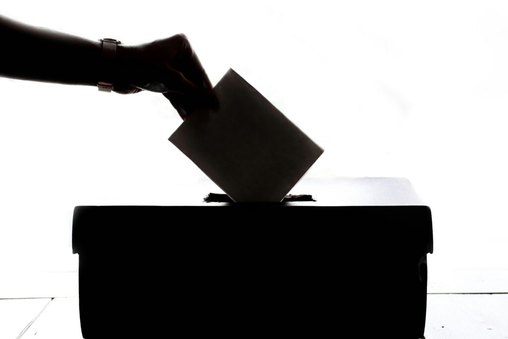 Eine Hand wirft einen Briefumschlag in eine schwarze Box mit Einwurfschlitz