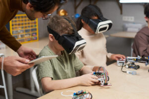 Zwei Kindern haben Virtual-Reality-Brillen auf, während sie am Tisch in der Klasse sitzen.