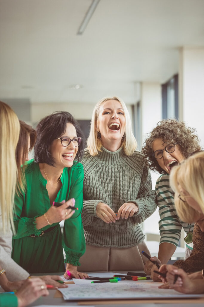 Eine Gruppe von Frauen beugt sich über ein Businesskonzept und lacht dabei.