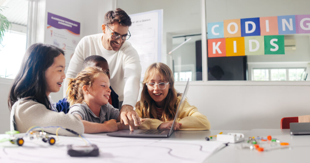 Ein männlicher Lehrer leitet Grundschüler in einem Codingkurs an.