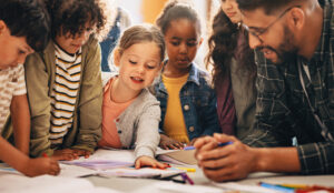 Eine Gruppe von Grundschulkindern lernt mit Hilfe ihrer Erzieherinnen das Zeichnen und Malen.