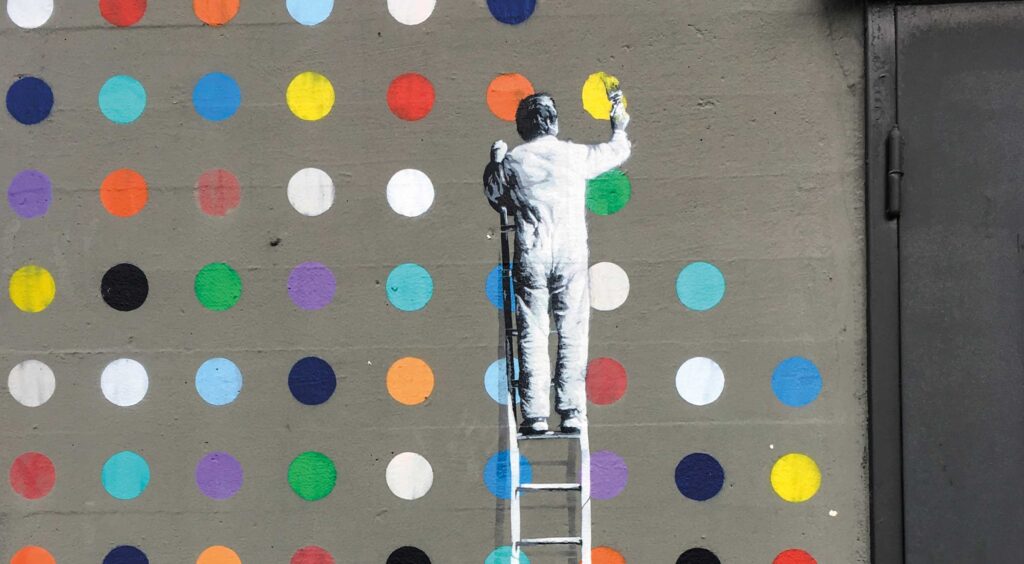 Graffiti an einer Wand, das einen Mann auf einer Leiter zeigt, der bunte Punkte auf die Wand malt
