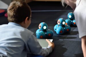 Zwei Kinder bringen kleine Roboter mit einem Tablet zum Fahren.