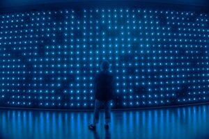 Eine junge Frau steht vor eimer Wand mit blau leuchtenden Buchstaben