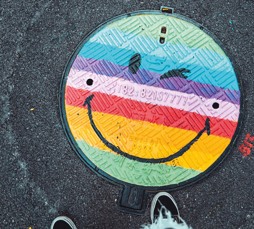 Gullideckel mit einem Aufdruck eines bunten Smileys