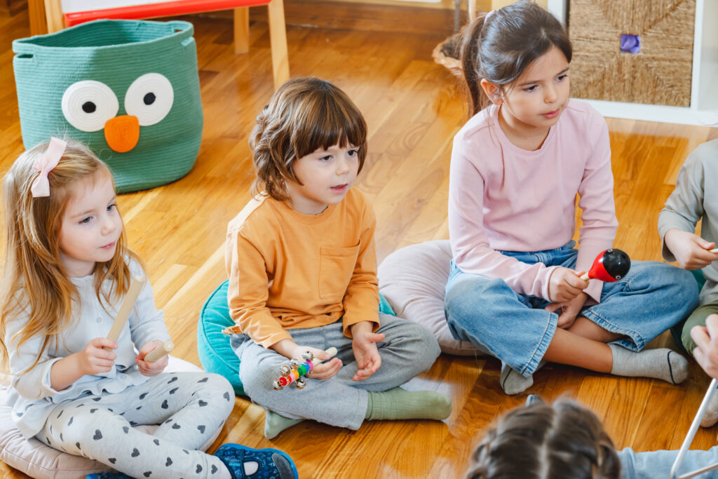 Kita-Kinder sitzen im Kreis auf dem Boden und halten Musikinstrumente in den Händen.