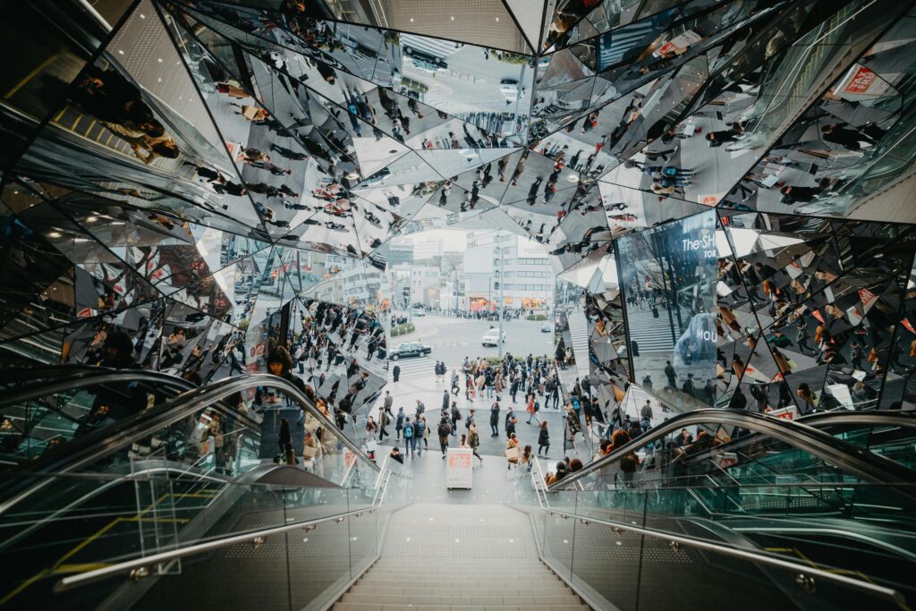 Der Blick geht von einer Treppe hinunter auf eine Straße. Die Decke ist verspiegelt, sodass sich alle Menschen darin doppeln.