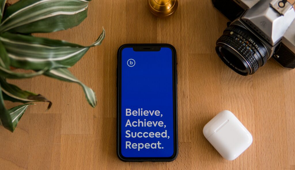 Ein Handy mit der Aufschrift "Believe, Achieve, Succeed, Repeat" liegt auf einem Tisch