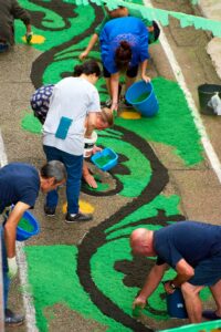 Viele Personen gestalten gemeinsam ein Kunstwerk auf dem Boden.