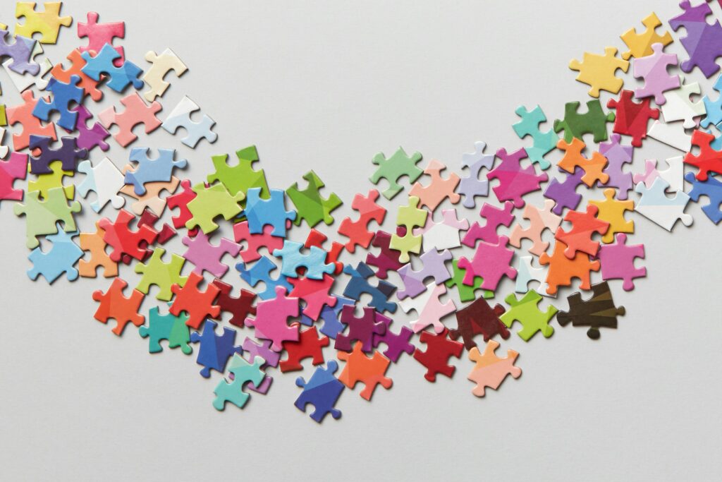 Viele verschiedene , bunte Puzzleteil liegen auf einem weißen Hintergrund.