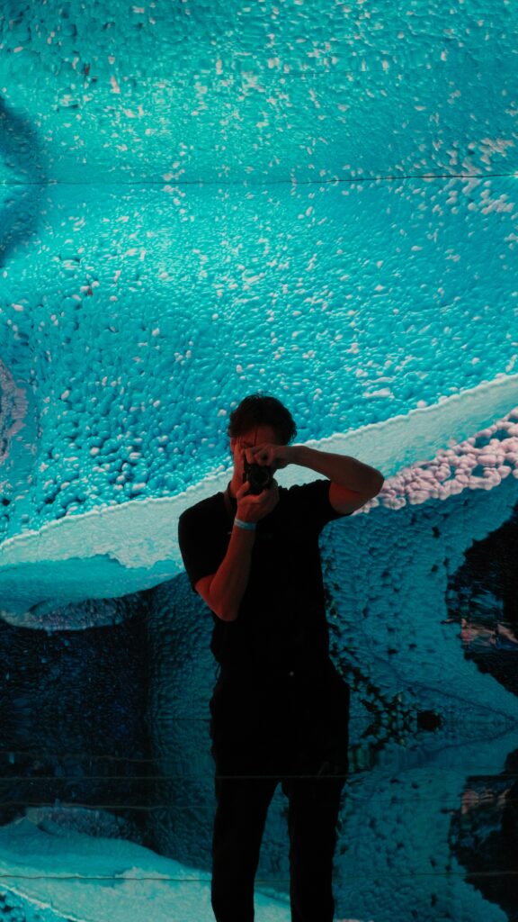 Ein junger Mann steht vor einer digital animierten Leinwand und fotografiert etwas.