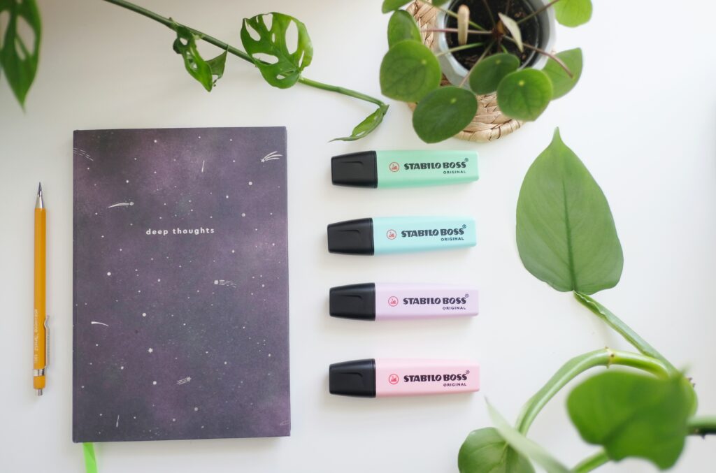 Auf einem Tisch liegen ein Notizblock, ein Bleistift und vier Textmarker