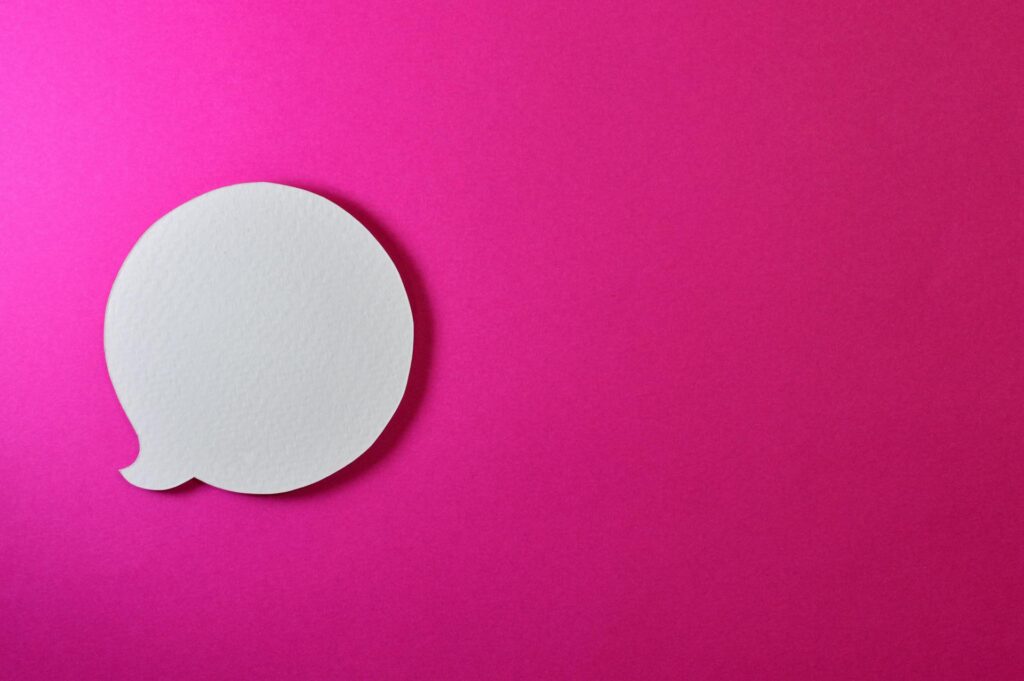 Eine weiße aus Papier ausgeschnittene Sprechblase ist vor einem rosa Hintergund platziert