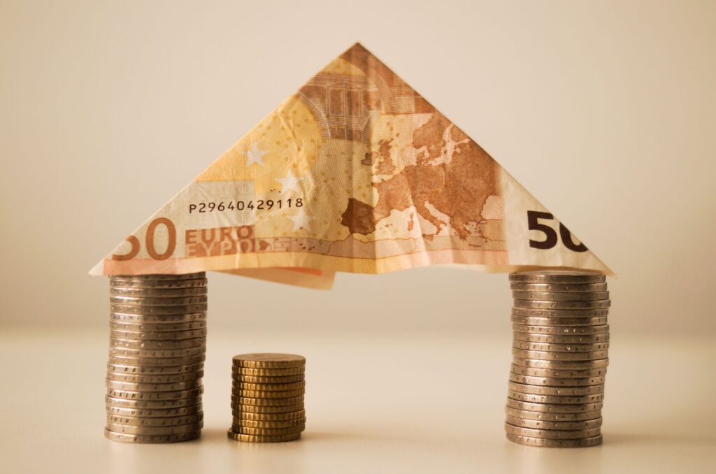 Auf zwei Staplen von Münzen ist ein gefalteter 50€ Schein aufgestellt.