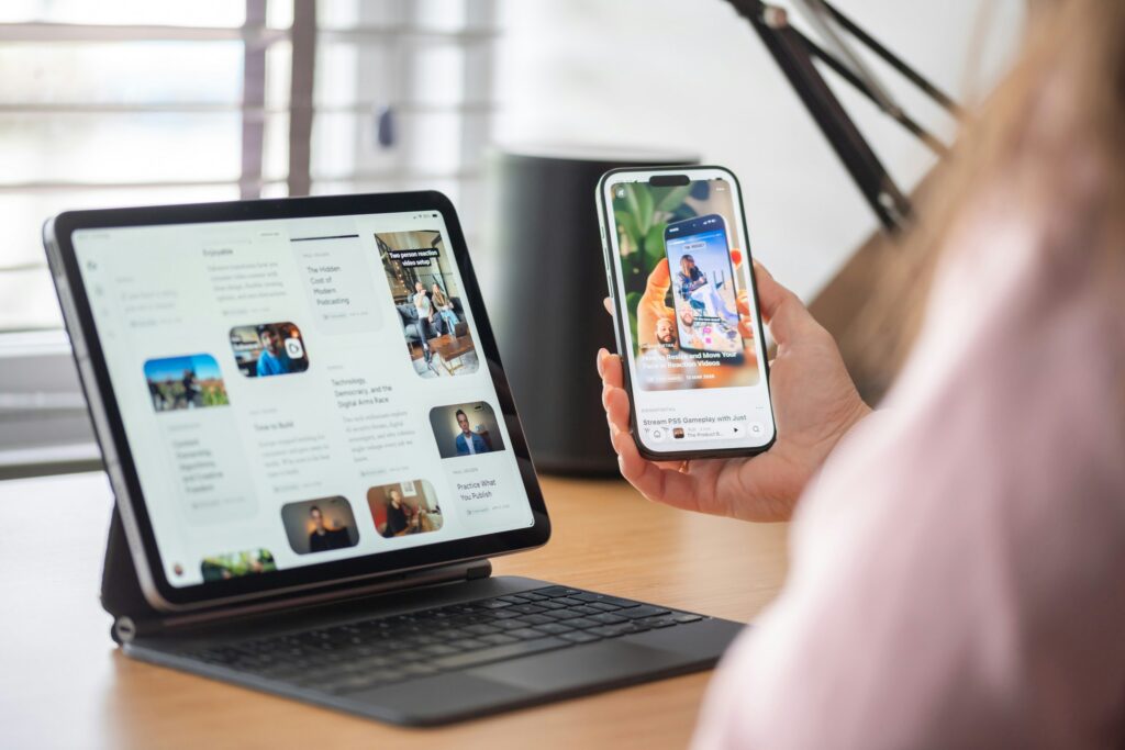 Eine Person sitzt vor einem Tablet und hält ein Handy in der Hand.